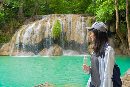 亚洲快乐妇女从热带森林瀑布的瓶子饮用水中在泰公园旅行和度假期间有树木自然高清图片素材