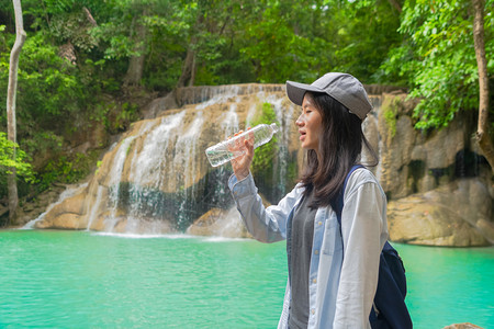 亚洲快乐妇女从热带森林瀑布的瓶子饮用水中在泰公园旅行和度假期间有树木自然的高清图片素材
