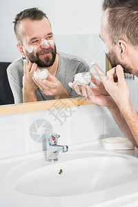 男人在浴室镜子前脸上涂满了香水男人在浴室里涂了润湿霜背景图片