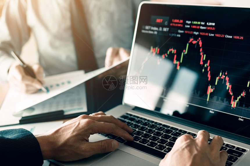 投资者正在使用笔记本电脑进入投资网站股票市场合作伙伴正在记录和分析业绩数据图片