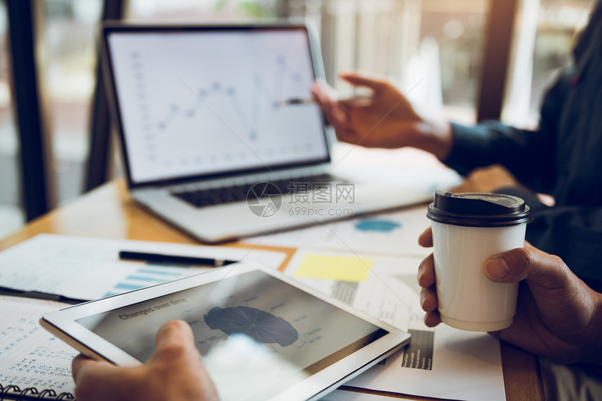 商业伙伴关系指向公司财务报表的图以及在计算机屏幕上赚取的利润向在办公室持有平板和咖啡的同事介绍情况图片