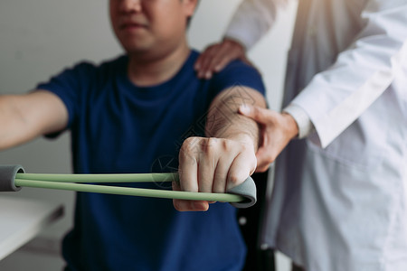 亚洲男理疗师血统与在诊疗室用灵活锻炼带进行伸展的病人一起工作背景图片