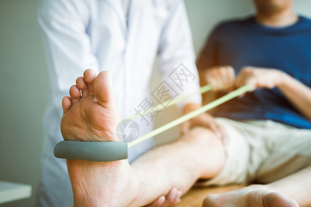 病人用抗药带伸展腿部身体治疗师在诊室帮忙背景图片