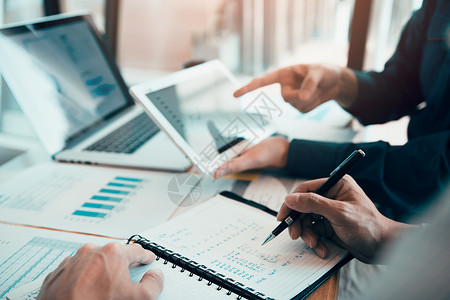 商业伙伴共同工作人员编写成本工作进度报告使用平板片分析公司财务预算报告图表和在办公室规划未来背景
