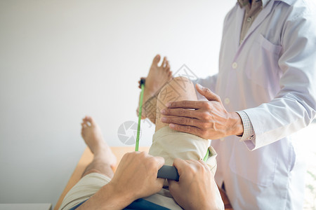 自信的理疗师帮助病人使用抗药带在诊疗室伸展腿部背景图片