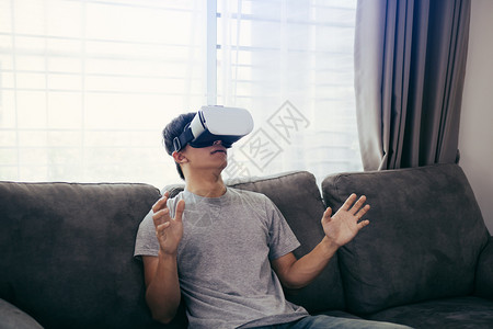 年轻的亚洲男子在客厅戴虚拟现实眼镜以欣赏虚拟现实沙发高清图片素材