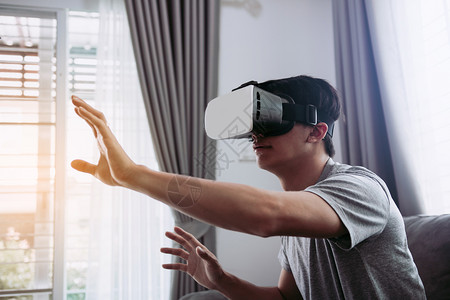 年轻的亚洲男子在客厅戴虚拟现实眼镜以欣赏虚拟现实背景高清图片素材
