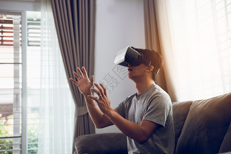 年轻的亚洲男子在客厅戴虚拟现实眼镜以欣赏虚拟现实手高清图片素材