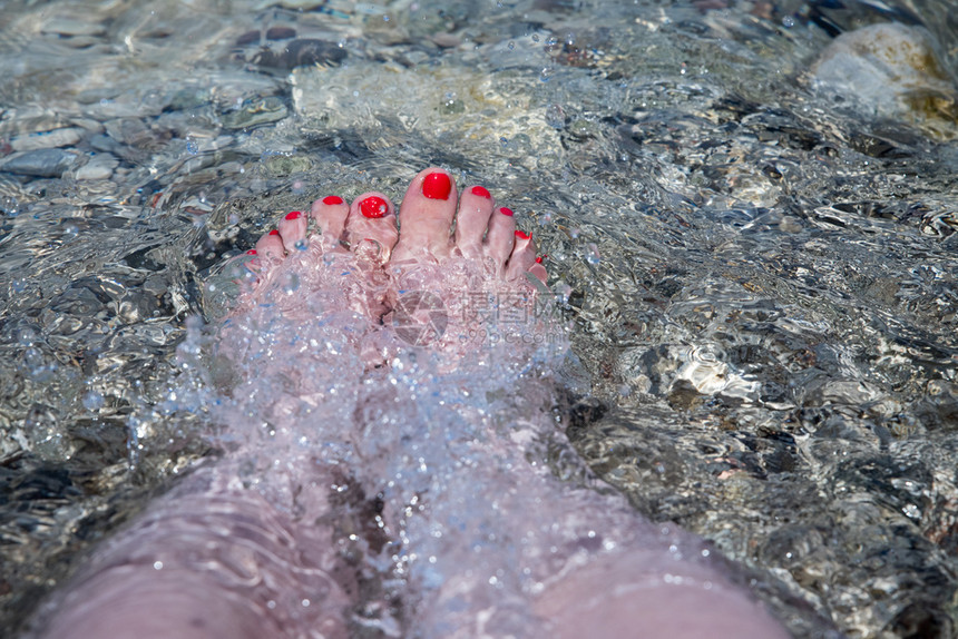 在水晶清海滩岸线中紧贴着有吸引力的女子脚加上红指甲油图片