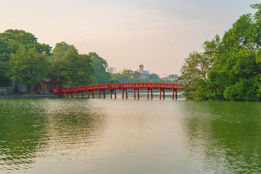 公园花中的红桥在河内市中心HoanKiem湖中间有树木和反射越南日落的城市景象背图片
