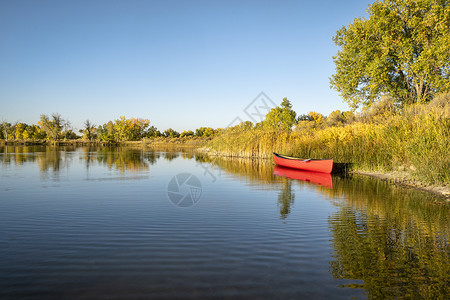 红色独木舟和一条划桨在平静的湖岸早期秋天风景背景图片