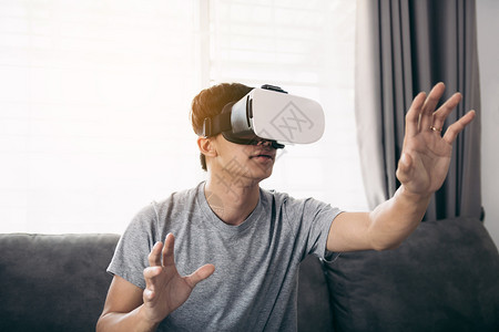 年轻的亚洲男子在客厅戴虚拟现实眼镜以欣赏虚拟现实聪明的高清图片素材