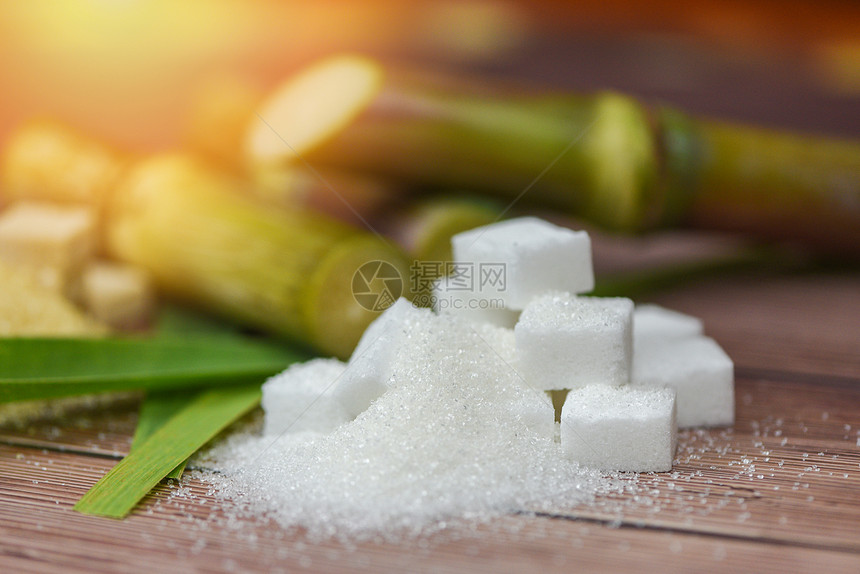 木制桌上的白糖立方和甘蔗以及阳光下的自然背景图片