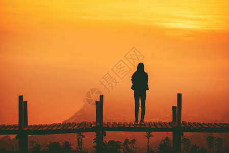 站在山的木桥上和黄的天空背景上女人图片