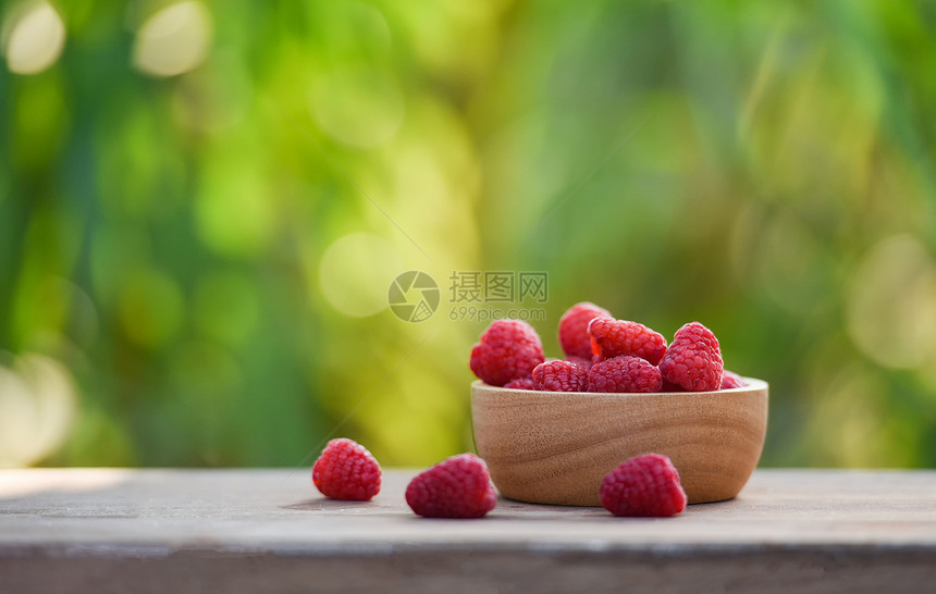 木碗中的新鲜树莓关闭红草莓果和自然绿色模糊背景图片