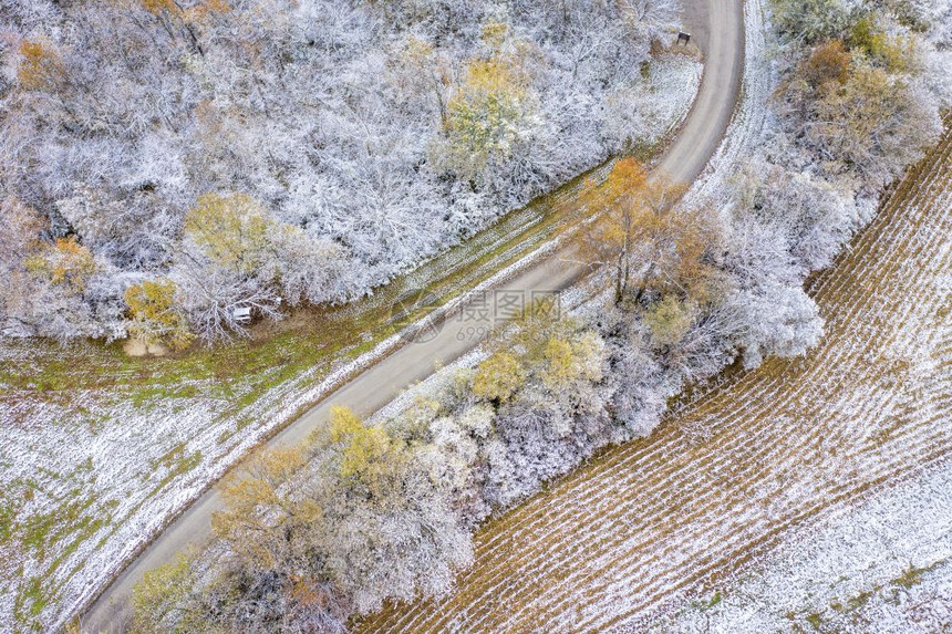 通过森林和收割的玉米田Windy砂砾路经过森林和收获的玉米田由早期积雪粉尘从空中观察密苏里西部的蜜溪保护区图片