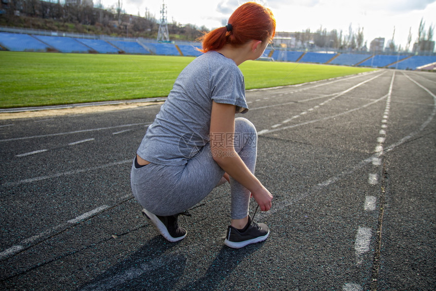年轻女孩准备在体育场跑步把鞋带绑在运动上图片