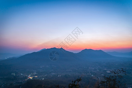 清晨村的日出风景山其背为橙色和蓝的天空在山上带有树林前景的山上背景图片