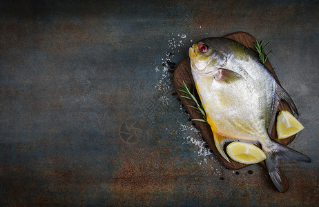 含有草药香料的新鲜乌黑鱼迷迭香和木制切板上的柠檬和黑底鱼原乌鱼背景图片