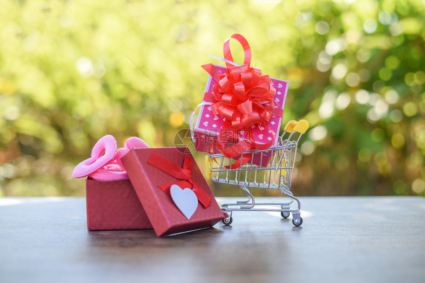 情人节购物和礼品箱粉红现货在购物车上贴红丝结弓在有自然户外的木上贴红开放礼品箱网上购物情人日概念图片
