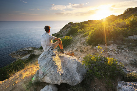一个人坐在山上的岩石看着日出太阳高清图片素材