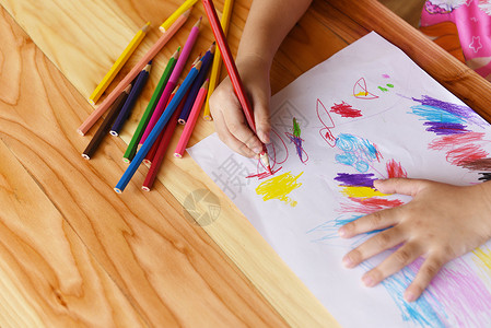 女孩在纸上画在家中木制桌上用彩色铅笔画孩子画和彩色蜡笔背景图片