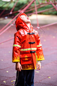 穿着红色消防员雨衣的有趣孩子在雨天公园玩耍儿童高清图片素材