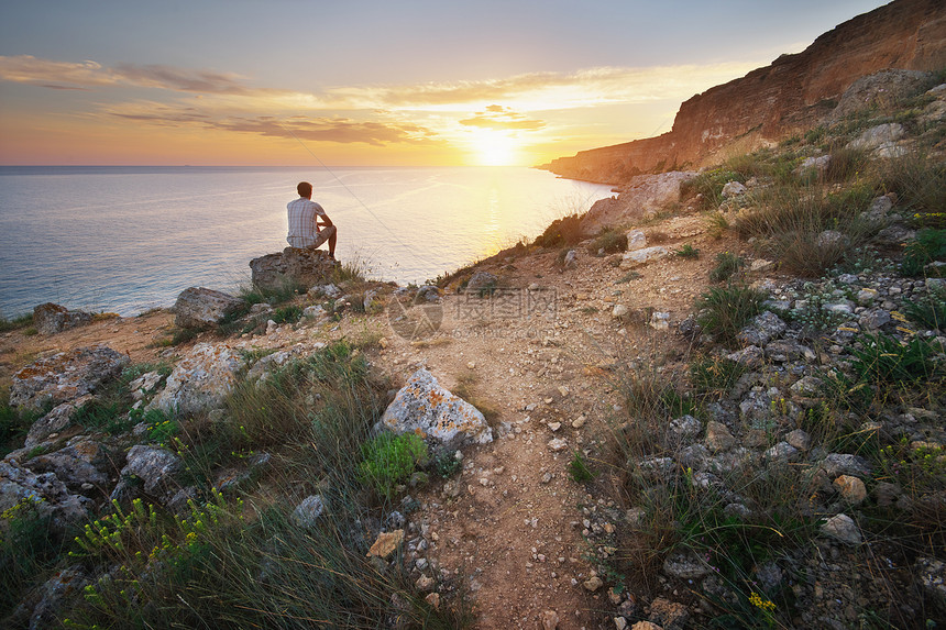 一个人坐在山上的悬崖看着日出的海浪自然构成图片