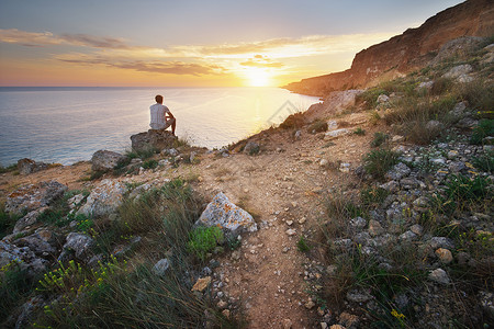 一个人坐在山上的悬崖看着日出的海浪自然构成生活方式高清图片素材