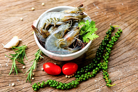 白碗新鲜虾和木制底配有食用海产品生虾的饲料草药和香图片