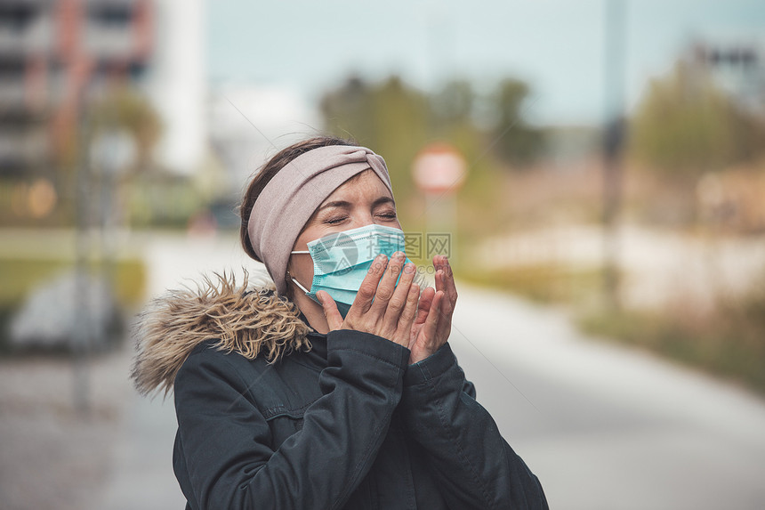穿面罩的在户外打喷嚏年轻女子科罗纳和流感季节图片