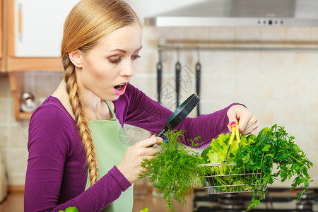 购买健康的饮食品概念厨房里的女人有很多绿色蔬菜她们通过放大镜看购物篮小车女人通过放大镜看蔬菜篮背景图片