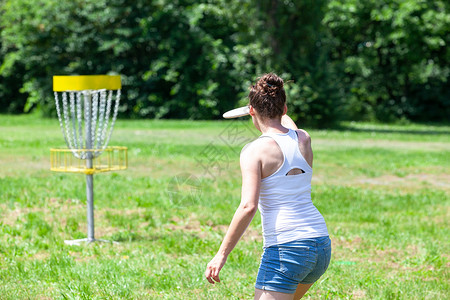 在公园里玩飞盘高尔夫运动游戏的年轻女子背景图片