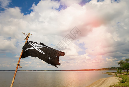 海盗旗素材黑褐色海盗旗JollyRoger身穿的殉难者在河流和阴云的天空背景下挥舞棍子黑色海盗旗背景