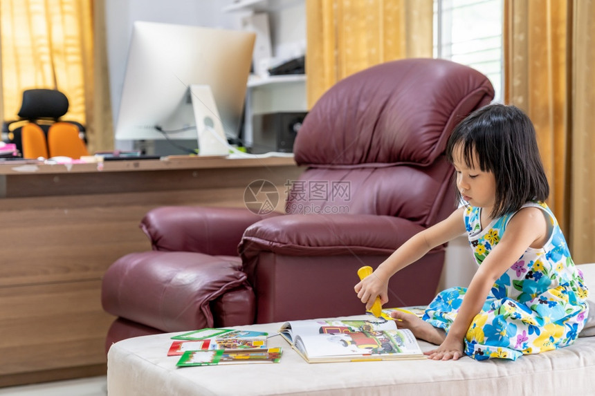 亚洲女童在家里客厅阅读互动式书作为家庭学校教育而城市则因为全世界可口的19大流行而被封锁图片