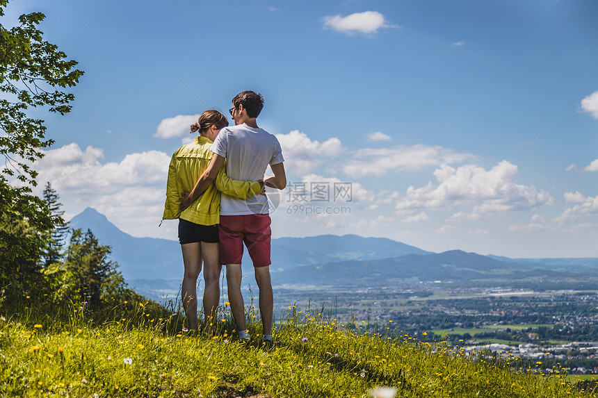 夫妇徒步旅行站在草地上享受远城风景图片