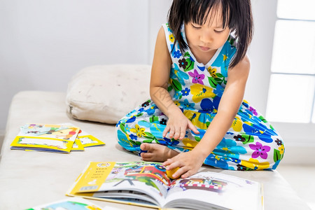 亚洲女童在家里客厅阅读互动式书作为家庭学校教育而城市则因为全世界可食19种流行病而被封锁家舍林为学龄前概念做准备背景图片
