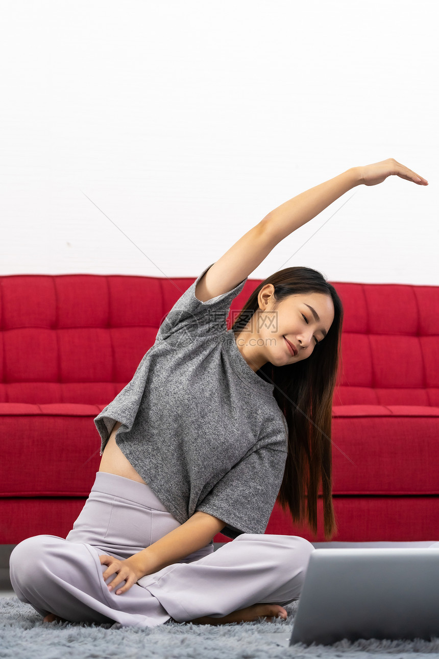 亚洲女使用笔记本电脑进行在线辅导以坐莲花姿势下锻炼运动活跃的年轻女在家里的客厅做伸展锻炼图片