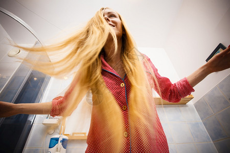 穿着睡衣在浴室的女人在梳她长金发时玩得开心从底部拍下来的法不同寻常图片