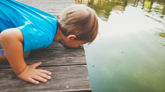 可爱的幼儿男孩在河边跪看着湖面漂浮的水流赤脚的高清图片素材