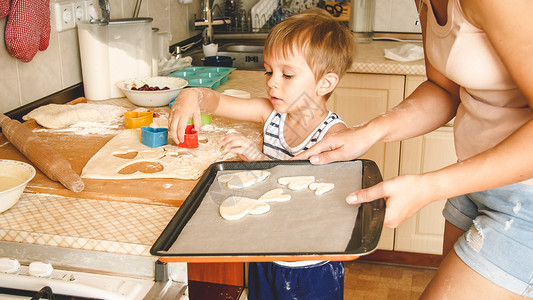 饼干男孩3岁幼儿男孩与母亲一起做饼干的近身肖像Child拿着烤锅并在上面贴饼干可爱3岁幼儿男孩与母亲一起做饼干的近身肖像背景