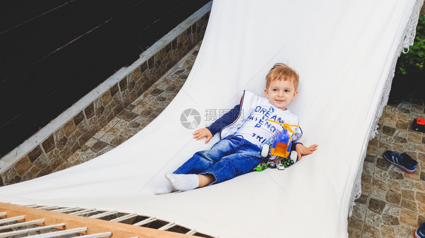照片来自3岁可爱的幼儿男孩他们躺在家后院的白色吊床上放松图片