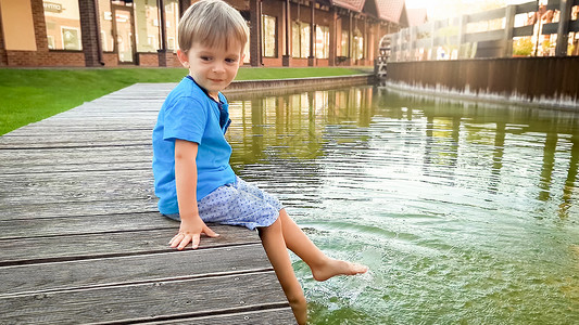 3岁可爱的小男孩在阳光夏日坐欧洲小镇的河岸上3岁可爱的幼儿男孩在阳光夏日坐欧洲小镇的河岸上池塘高清图片素材