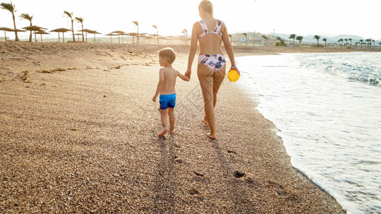 照片快乐的年轻母亲与可爱的3岁幼儿男孩手牵在海滨与水面美丽的日落天空对面行走图片快乐的年轻母亲与可爱的3岁幼儿男孩手牵在海边与美情绪高清图片素材