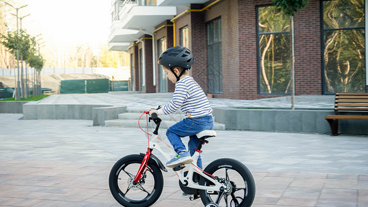 快乐的小男孩穿着头盔在城市街道上骑着第一辆自行车学习图片