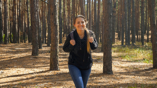 呜呜呜带着背包徒步和秋天在森林中行走的快乐微笑年轻女肖像背景