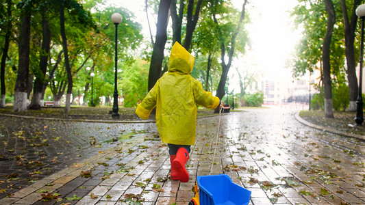 雨桶雨天在公园穿雨衣拿绳子拖玩具卡车的男孩背景