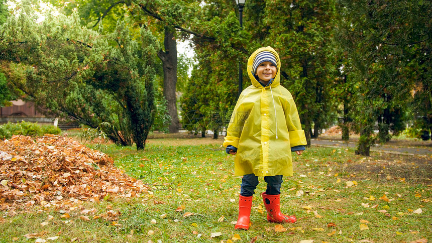 快乐的男孩在公园下雨后穿着黄色衣和红橡皮靴图片