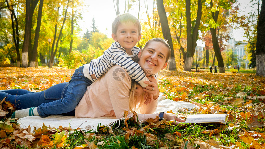 快乐笑的小男孩躺在秋天公园的母亲上图片