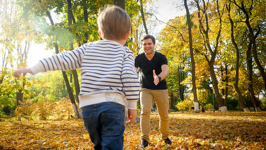 小孩男跑到秋天公园的他笑着父亲那里去图片